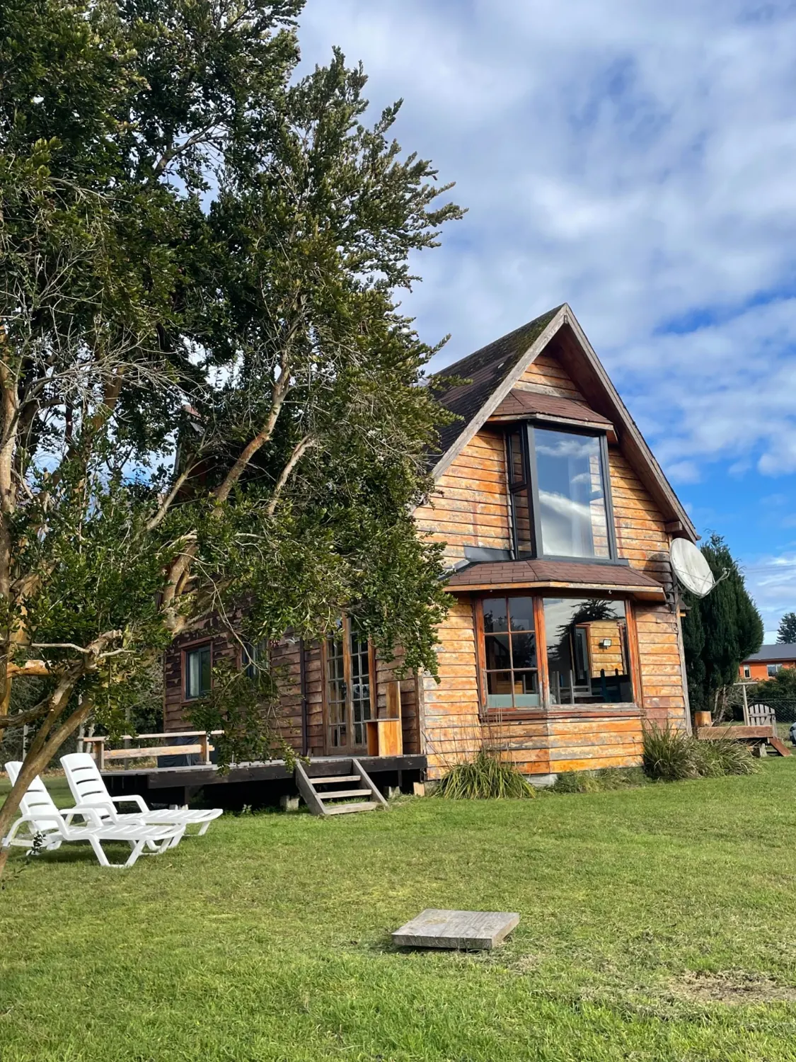 Fachada de madera de la casa con ventanal, terraza y reposeras en el jardín