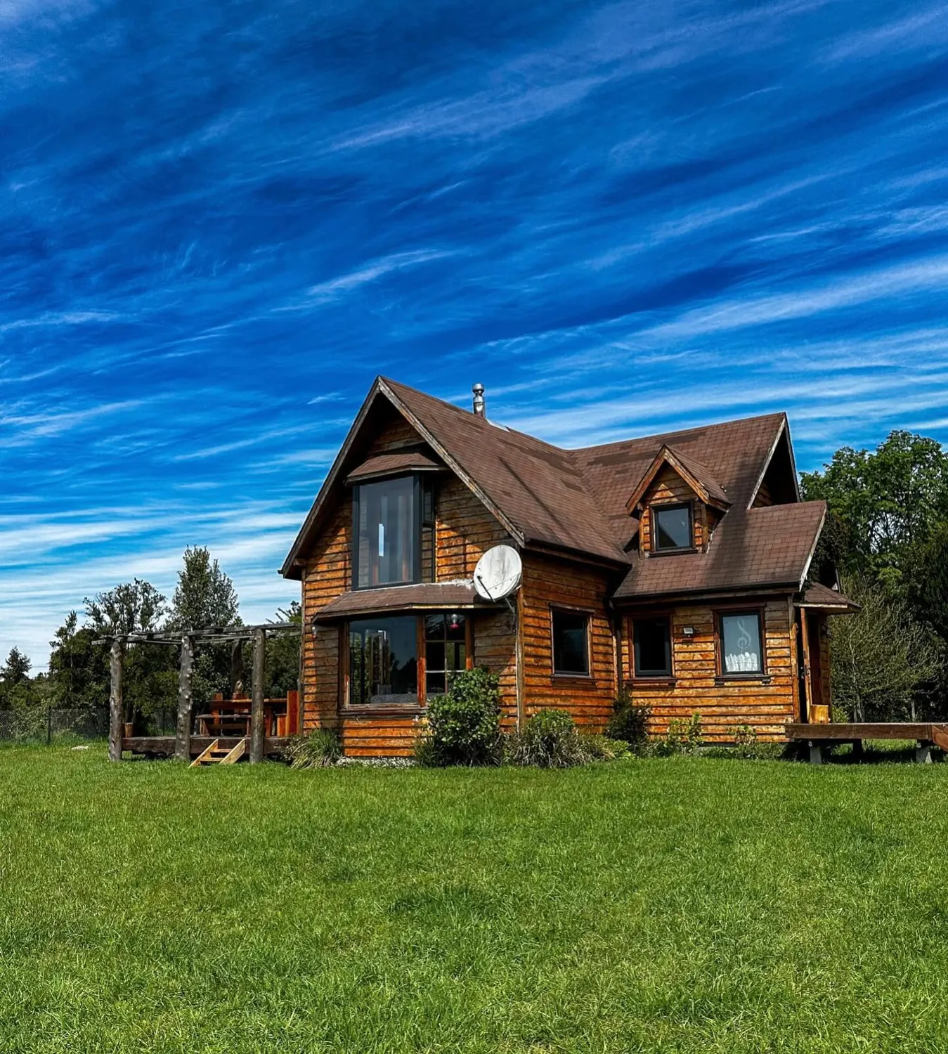 Casa de Cuentos, casa de madera nativa rodeada de pasto verde bajo un cielo azul, en Frutillar